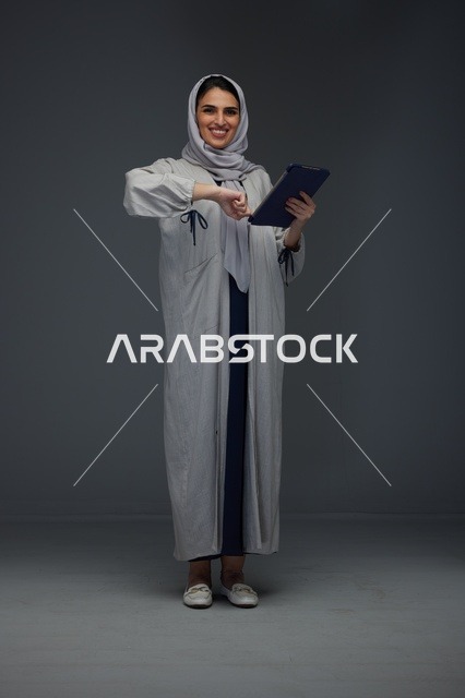 امرأة سعودية مبتسمة تستخدم جهاز لوحي في الاستوديو