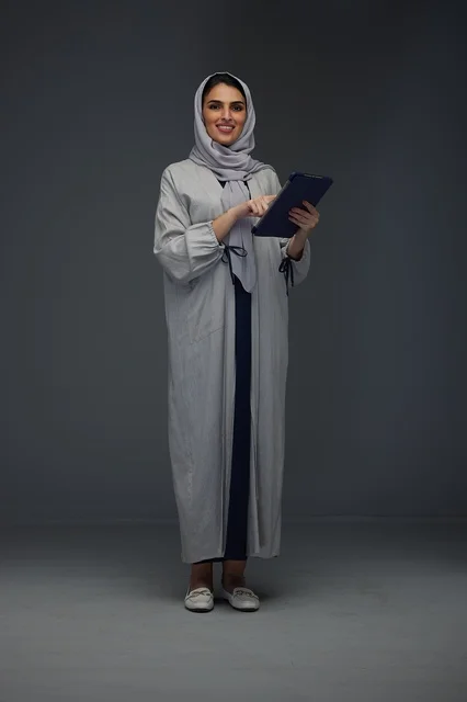 امرأة سعودية بعباءة رمادية تستخدم جهازاً لوحياً