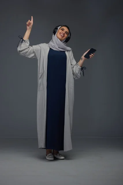 Saudi Woman with Headphones and Smartphone on Grey Background