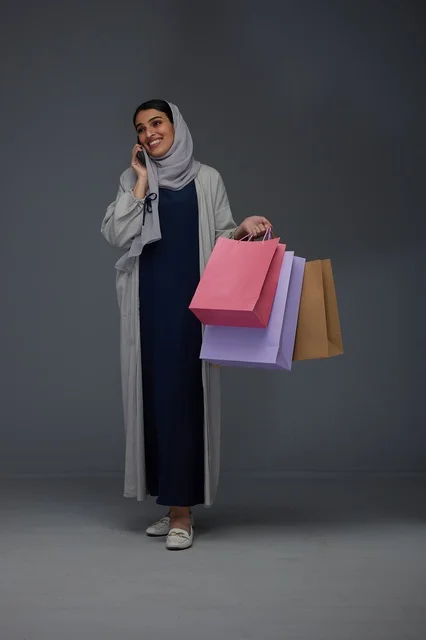 امرأة سعودية تتسوق وتحمل حقائب وتتحدث بالهاتف المحمول