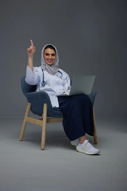 طبيبة سعودية مع كمبيوتر محمول تشير للأعلى في استوديو