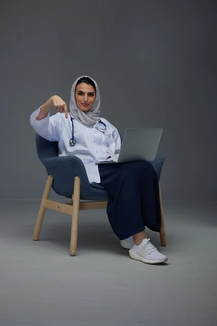 طبيبة سعودية تجلس مع كمبيوتر محمول وتشير لأسفل