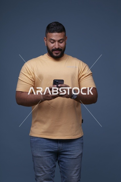 رجل سعودي يستخدم الهاتف الذكي في استوديو بخلفية زرقاء