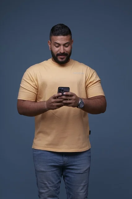 رجل سعودي يستخدم الهاتف الذكي في استوديو بخلفية زرقاء