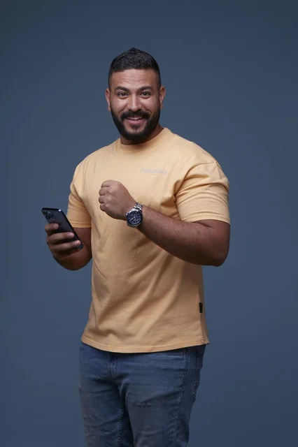 رجل سعودي بملابس كاجوال يحمل هاتف ذكي بإيماءة نجاح
