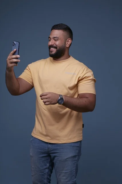 رجل سعودي مبتسم يستخدم الهاتف الذكي بخلفية زرقاء