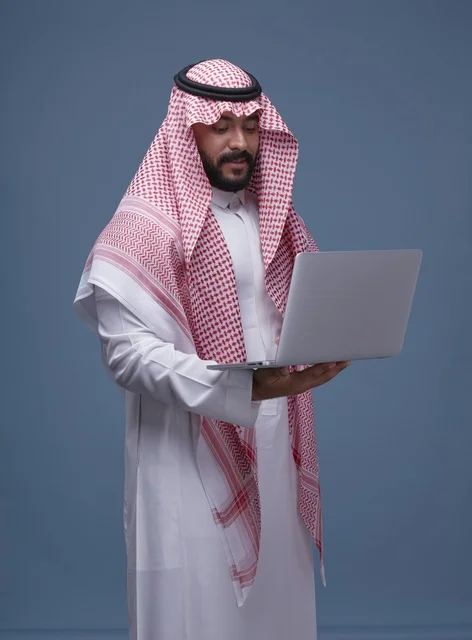 رجل سعودي بالزي التقليدي يستخدم حاسوب محمول في استوديو