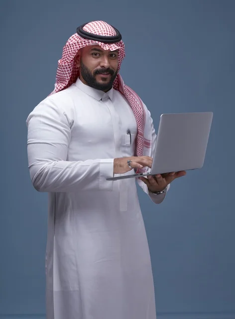 رجل سعودي بالزي التقليدي يستخدم الحاسوب