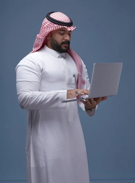 رجل سعودي بالزي التقليدي يستخدم حاسوب محمول في استوديو