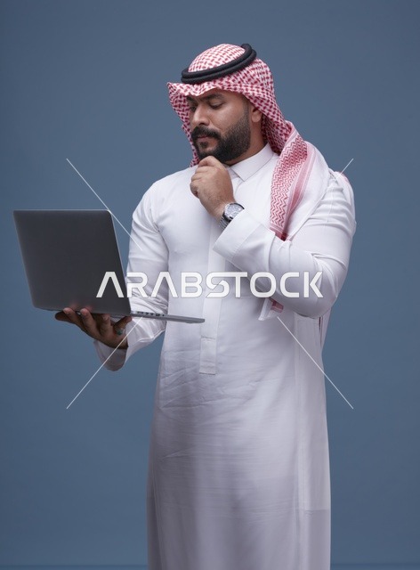 رجل سعودي يستخدم الحاسوب المحمول بالزي التقليدي