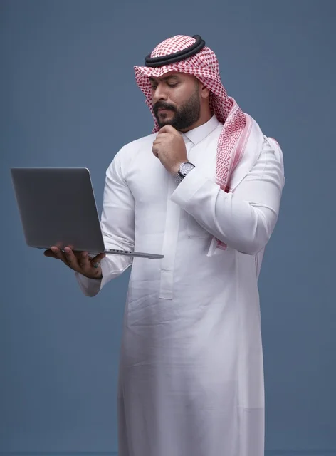 رجل سعودي يستخدم الحاسوب المحمول بالزي التقليدي