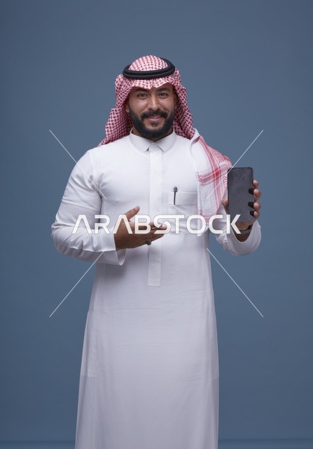 رجل سعودي يحمل هاتفاً ذكياً بشاشة فارغة