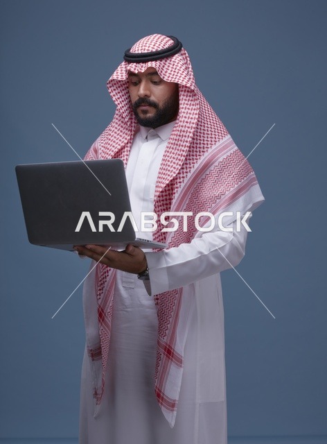 رجل سعودي يستخدم حاسوب محمول بالزي التقليدي في الاستوديو