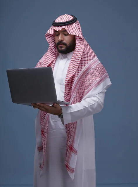 رجل سعودي يستخدم حاسوب محمول بالزي التقليدي في الاستوديو