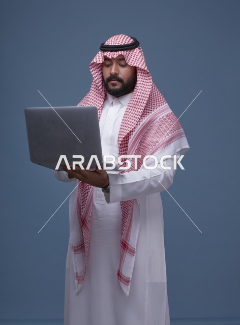 رجل سعودي يستخدم حاسوب محمول بالزي التقليدي في استوديو