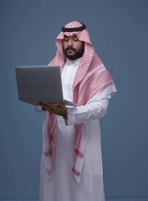رجل سعودي يستخدم حاسوب محمول بالزي التقليدي في استوديو