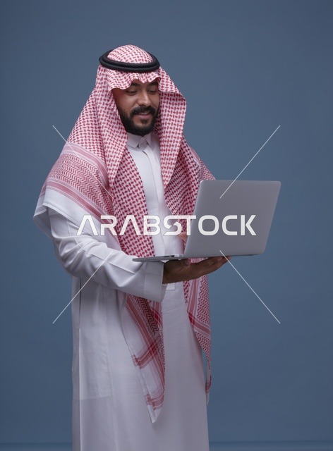 رجل سعودي مع حاسوب محمول بالزي التقليدي في استوديو