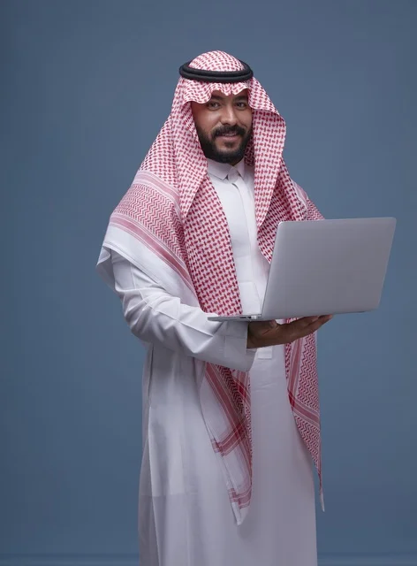 رجل سعودي بالزي التقليدي يستخدم حاسوب محمول في استوديو