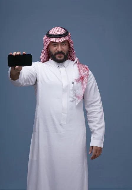 رجل سعودي بالزي التقليدي يحمل هاتفاً ذكياً بشاشة فارغة