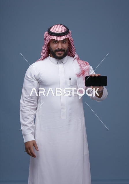 رجل سعودي بالزي التقليدي يحمل هاتفاً بشاشة فارغة