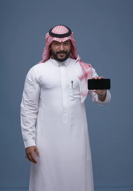 رجل سعودي بالزي التقليدي يحمل هاتفاً بشاشة فارغة