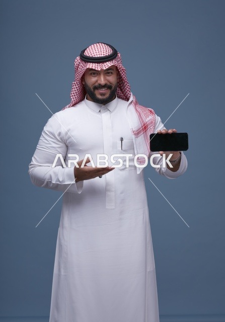 رجل سعودي يحمل هاتف ذكي بشاشة فارغة بالزي التقليدي