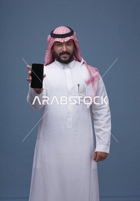 رجل سعودي يحمل هاتفاً بشاشة فارغة في الاستوديو