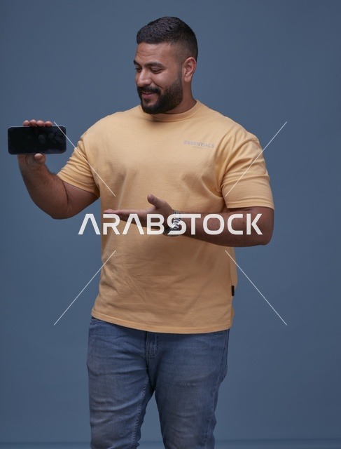 رجل سعودي مبتسم يحمل هاتف ذكي بشاشة فارغة خلفية زرقاء