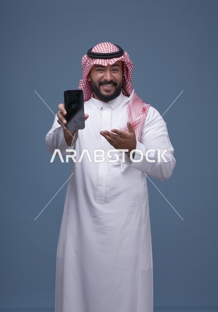 رجل سعودي يحمل هاتف ذكي بشاشة فارغة في استوديو