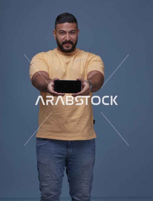 رجل سعودي مبتسم يعرض شاشة هاتف فارغة بملابس كاجوال