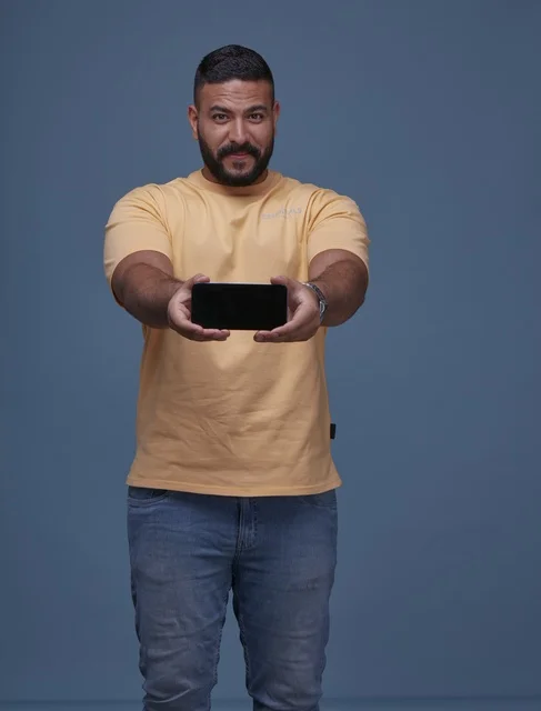 Smiling Saudi Man Showing Blank Smartphone Screen in Casual Outfit