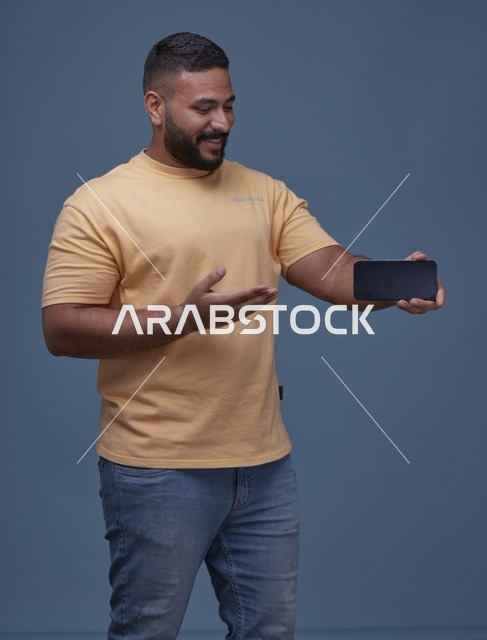 رجل سعودي يحمل هاتف ذكي بشاشة فارغة خلفية زرقاء