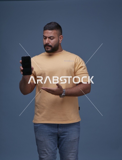 رجل سعودي يحمل هاتف ذكي بشاشة فارغة في الاستوديو