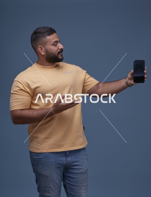 رجل سعودي يحمل شاشة هاتف فارغة بخلفية زرقاء