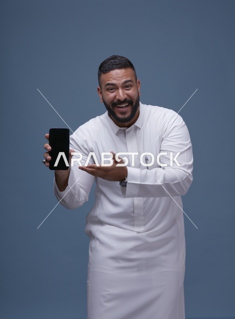 رجل سعودي يرتدي الثوب الأبيض ويحمل هاتف ذكي بشاشة فارغة
