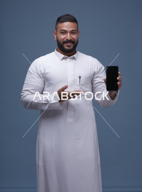 رجل سعودي بالثوب الأبيض يحمل هاتفاً بشاشة فارغة