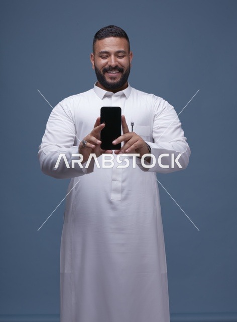 رجل سعودي يرتدي ثوباً أبيض يحمل هاتفاً بشاشة فارغة