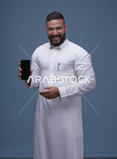 رجل سعودي بالثوب الأبيض يحمل هاتفاً ذكياً بشاشة فارغة