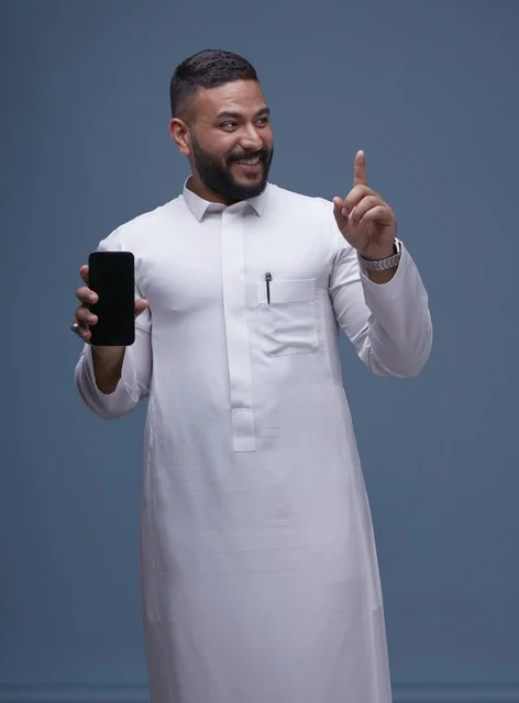 رجل سعودي بالثوب الأبيض يحمل هاتفاً بشاشة فارغة