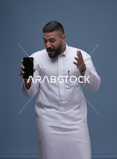 رجل سعودي مندهش يمسك هاتف ذكي بشاشة فارغة