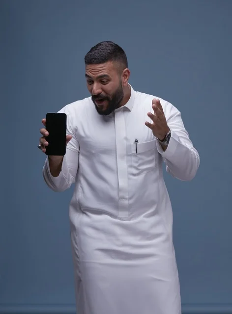 رجل سعودي مندهش يمسك هاتف ذكي بشاشة فارغة