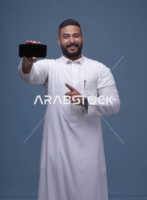 رجل سعودي بالثوب الأبيض يحمل هاتف ذكي بشاشة فارغة