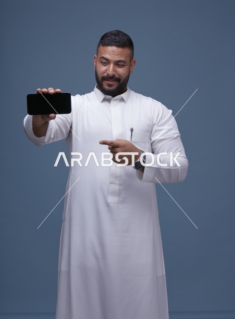 رجل سعودي بالثوب الأبيض يشير لشاشة هاتف فارغة