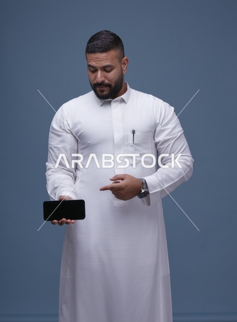رجل سعودي يرتدي الثوب الأبيض يحمل هاتفاً بشاشة فارغة