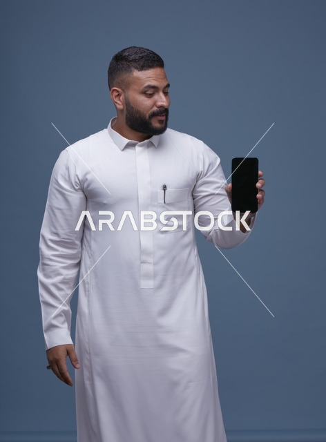 رجل سعودي بالثوب الأبيض يحمل هاتف بشاشة فارغة