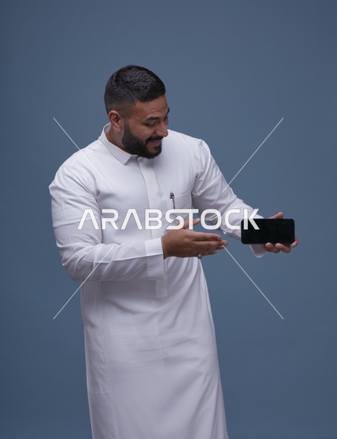 رجل سعودي بالثوب الأبيض يحمل هاتف ذكي بشاشة فارغة