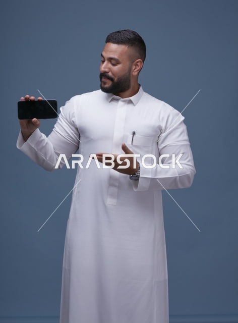 رجل سعودي بالثوب الأبيض يعرض شاشة هاتف ذكي فارغة