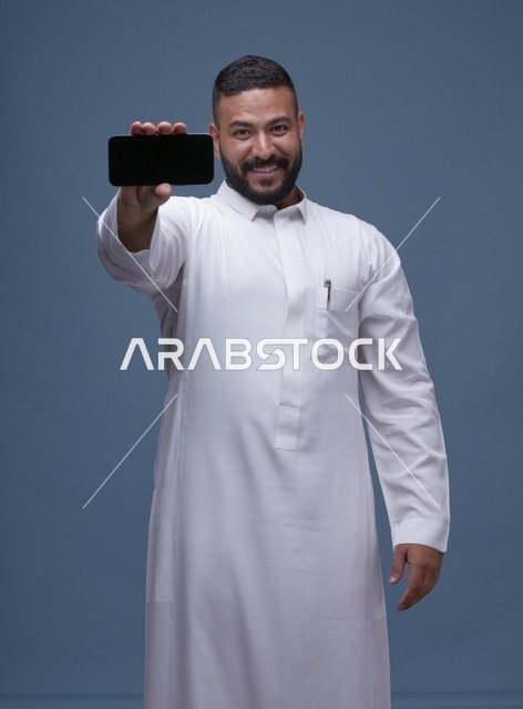 رجل سعودي بالثوب الأبيض يحمل هاتف ذكي بشاشة فارغة