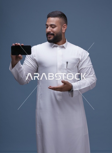 رجل سعودي بالثوب الأبيض يعرض شاشة جوال فارغة