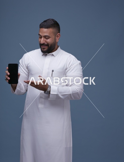 رجل سعودي بالثوب الأبيض يحمل هاتف محمول بشاشة فارغة